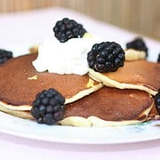 Vintage floral china plate with pancakes topped with whipped cream and blavkberries.