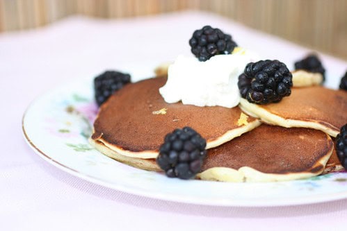 Vintage floral china plate with pancakes topped with whipped cream and blavkberries.
