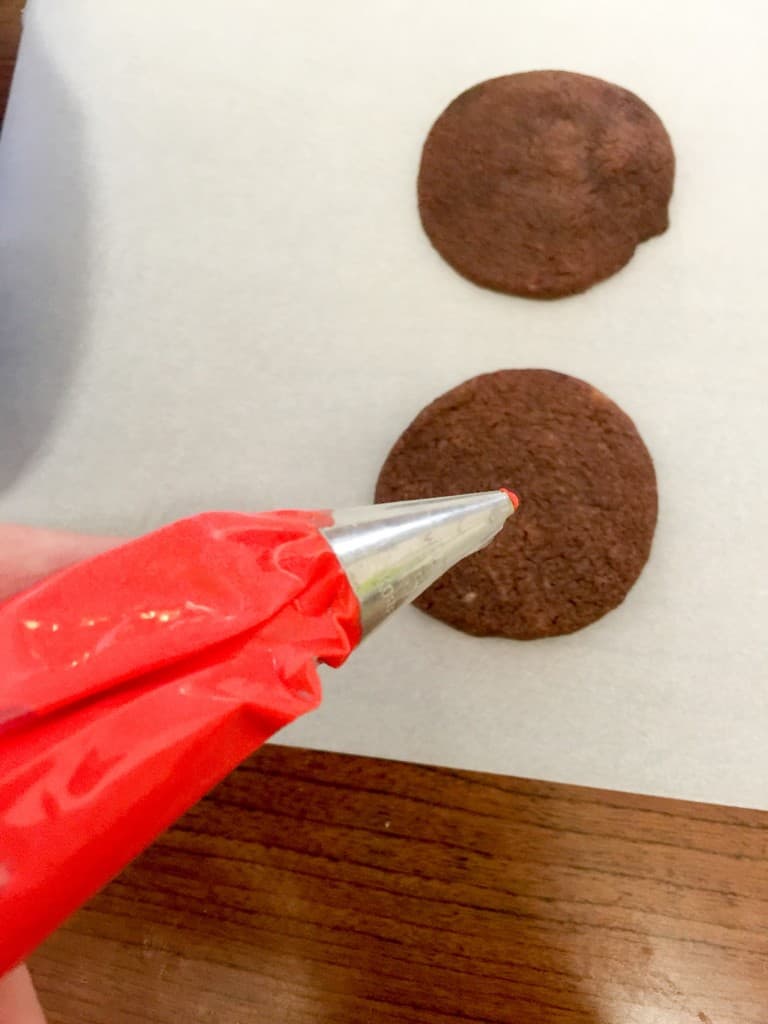 Piping bag over a dark chocolate shortbread cookie on a tray