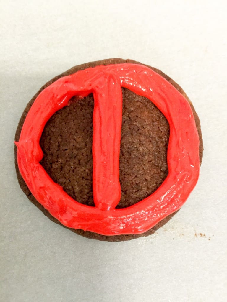 Dark chocolate shortbread cookie with the outline of deadpool piped on to it.