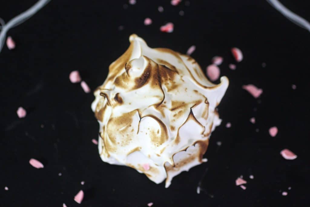 Mini Baked Alaska sitting on a chalkboard with peppermint sprnkles.