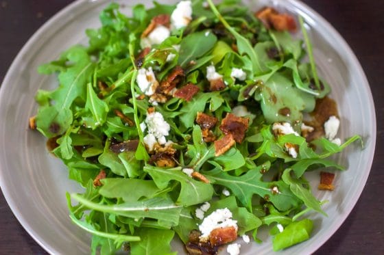 Grey plate holding arugula salad with warm bacon vinaigrette and goat cheese