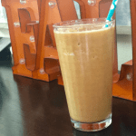 Glass filled with Pumpkin Spice Protein Shake in front of a fall sign.