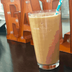 Glass filled with Pumpkin Spice Protein Shake in front of a fall sign.