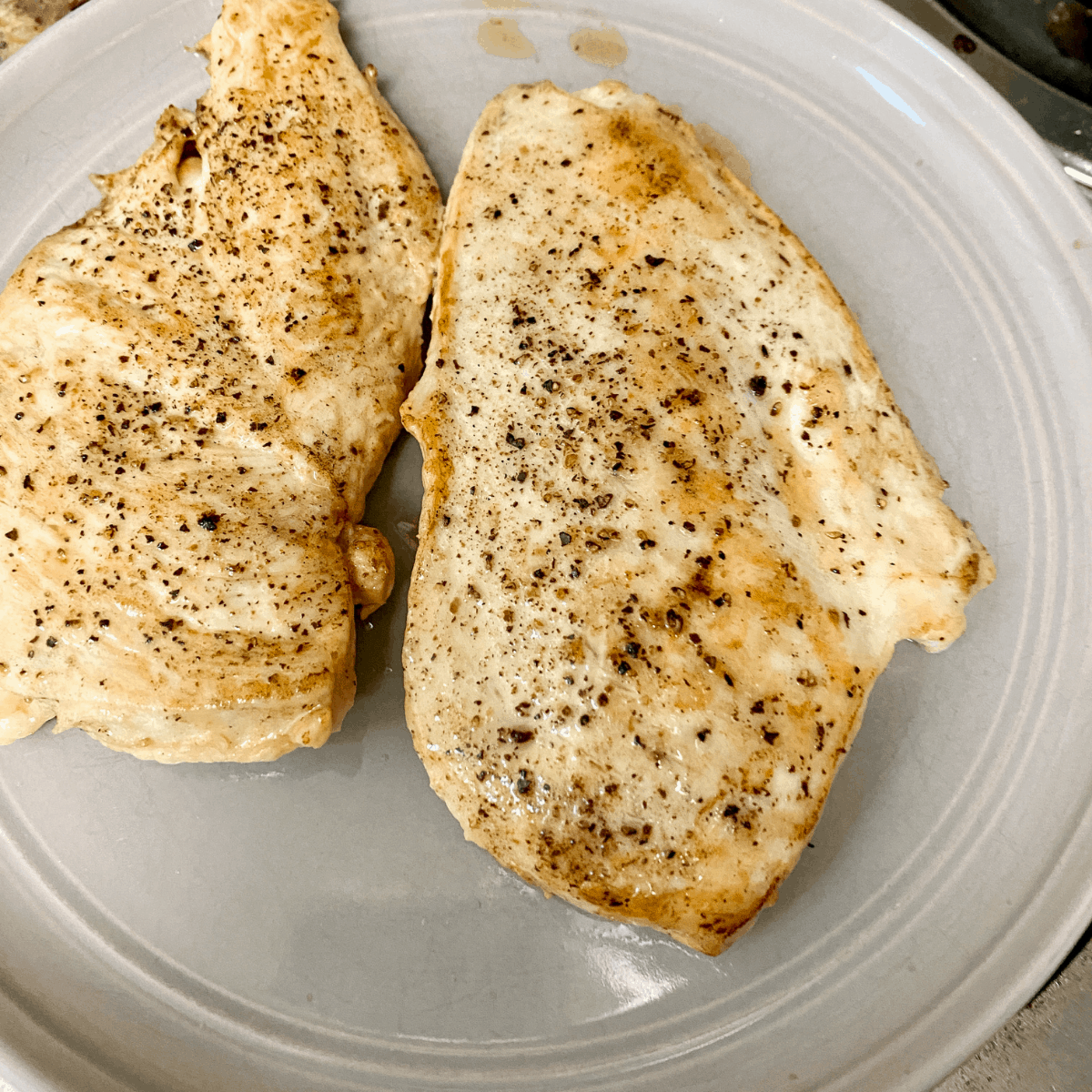 Two sauteed breasts of chicken on a grey plate.