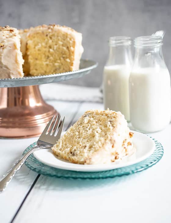 cake on a cake platter with a slice of maple pecan chiffon cake and two containers of milk.