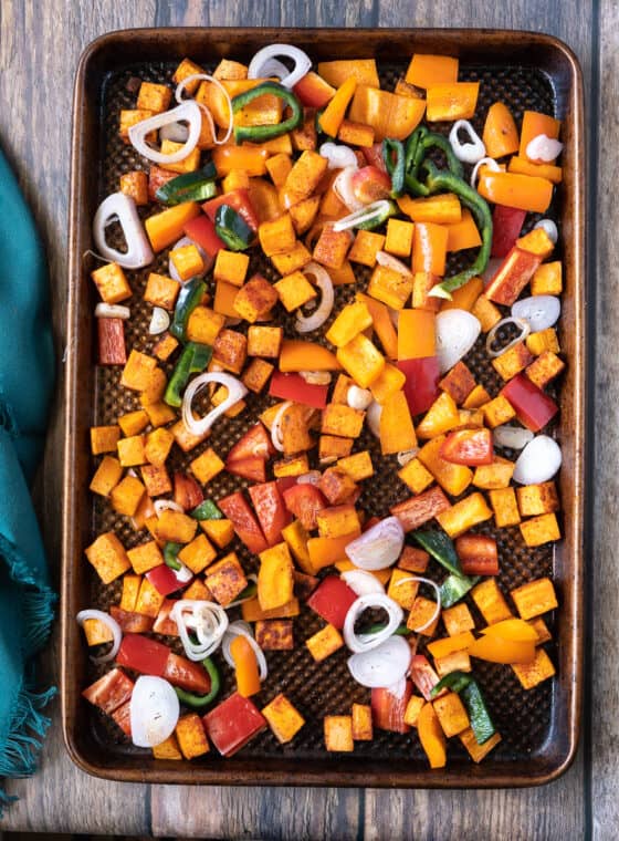 Sheet pan of sweet potatoes, poblano peppers, shallots and red peppers ready to roast.
