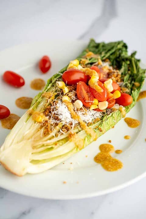 White plate with half a romaine heart grilled and topped with spicy caesar vinaigrette.