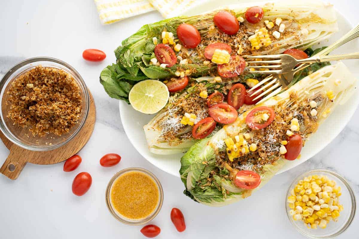 Plate with Grilled romaine salad with the dressing, breadcrumbs and corn on the side.