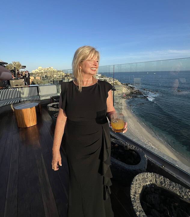 Cheri Liefeld standing on a balcony at sunset overlooking cabo beach.