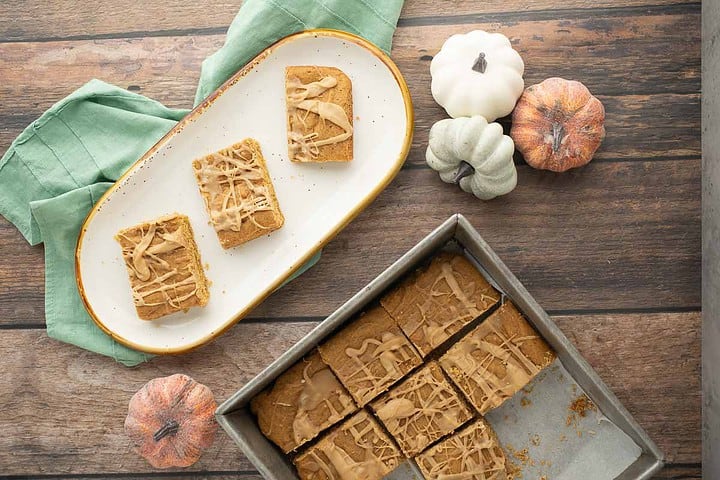 Overview of plate of maple pumpkin butter bars in a square pan and a white platter with three cut bars on there.